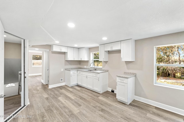 kitchen with white cabinets, light wood-type flooring, light stone counters, and sink