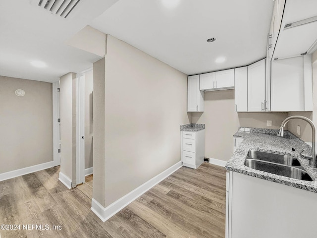 kitchen with light stone countertops, sink, white cabinets, and light wood-type flooring