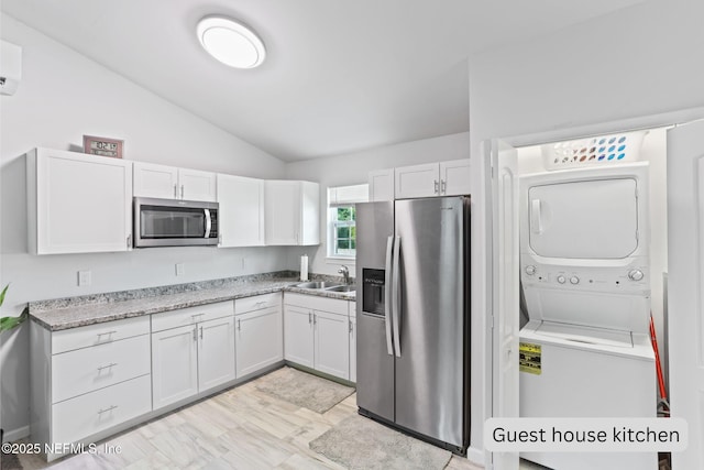 kitchen with appliances with stainless steel finishes, stacked washing maching and dryer, vaulted ceiling, sink, and white cabinets