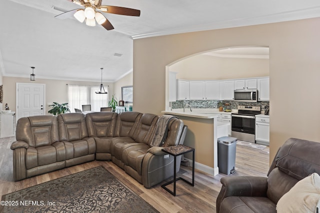 living room featuring sink, ornamental molding, vaulted ceiling, ceiling fan with notable chandelier, and light wood-type flooring