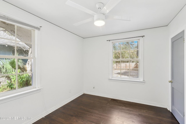 empty room with dark wood-style floors, visible vents, plenty of natural light, and baseboards