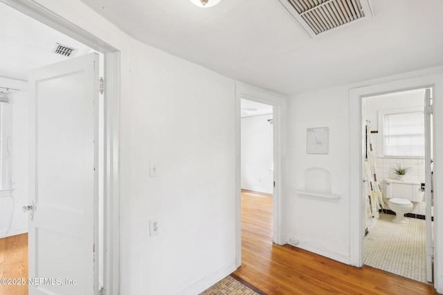 corridor featuring visible vents, baseboards, and wood finished floors