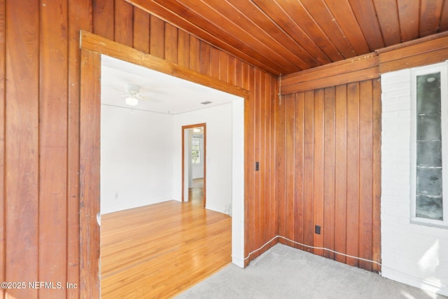 empty room with light carpet, wooden ceiling, wooden walls, and a ceiling fan