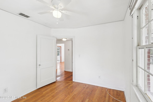 empty room featuring a ceiling fan, light wood-type flooring, visible vents, and baseboards