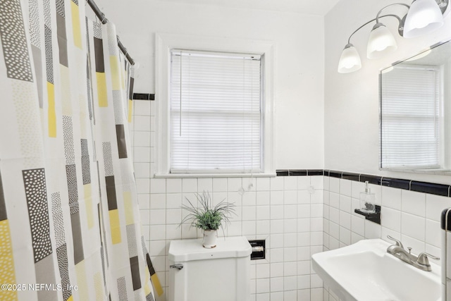 bathroom with a wainscoted wall, tile walls, a shower with shower curtain, toilet, and a sink