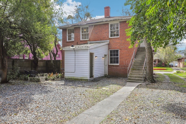 back of house featuring brick siding, fence, a chimney, and stairs