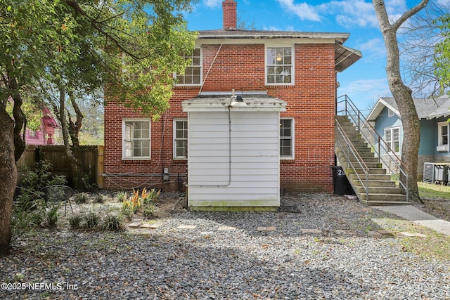 back of property with stairs, a chimney, fence, and brick siding