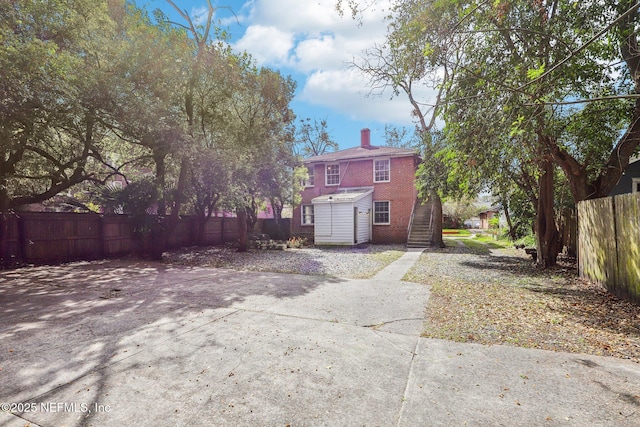 back of house with brick siding, a chimney, stairway, fence, and an outdoor structure