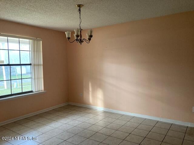 tiled empty room with a wealth of natural light, a textured ceiling, and an inviting chandelier