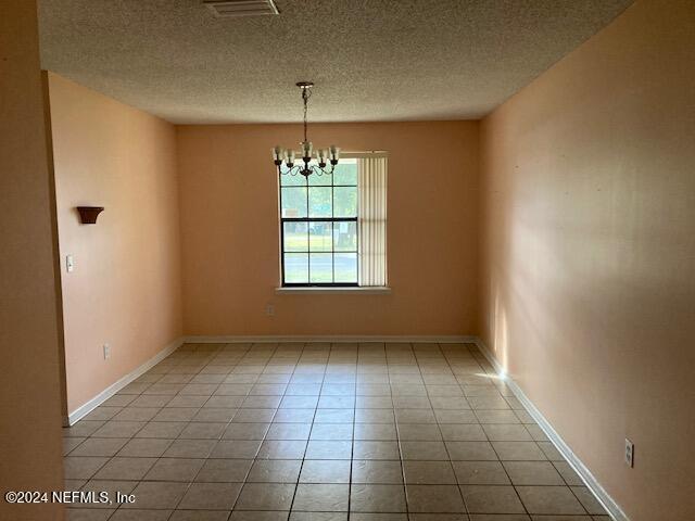 unfurnished room featuring light tile patterned floors, a chandelier, and a textured ceiling