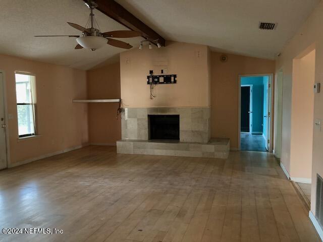 unfurnished living room with a tile fireplace, ceiling fan, light hardwood / wood-style flooring, and lofted ceiling with beams