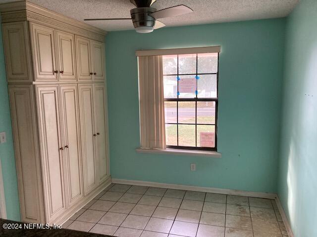 interior space featuring ceiling fan, light tile patterned flooring, and a textured ceiling