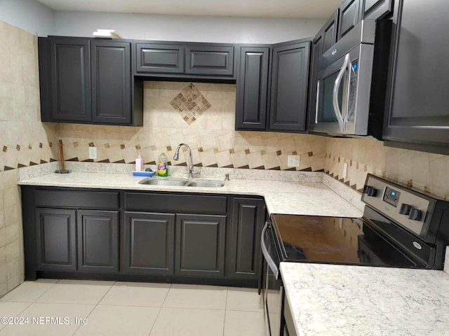 kitchen featuring dark cabinetry, appliances with stainless steel finishes, backsplash, and a sink