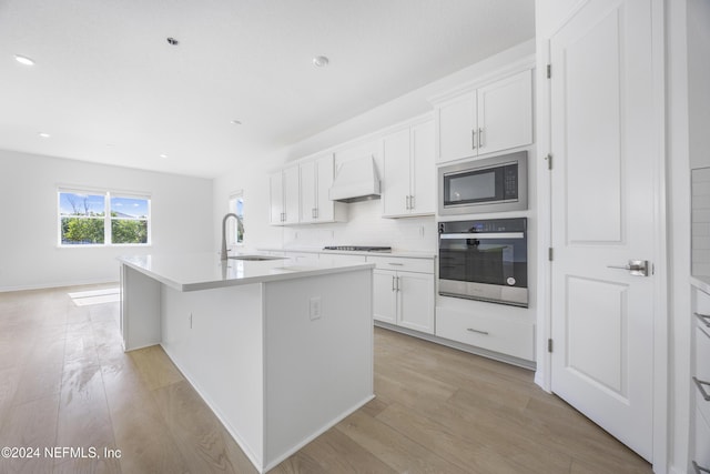 kitchen with premium range hood, stainless steel oven, black microwave, a kitchen island with sink, and sink