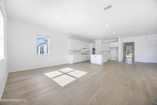 unfurnished living room with sink, a healthy amount of sunlight, and light hardwood / wood-style floors