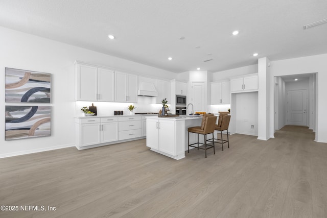 kitchen with white cabinetry, a kitchen island with sink, custom range hood, and a kitchen breakfast bar