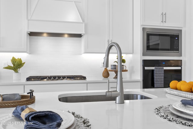 kitchen with oven, stainless steel microwave, custom range hood, sink, and white cabinets