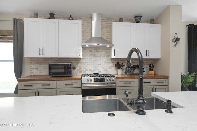 kitchen with decorative backsplash, stainless steel gas range oven, wall chimney range hood, white cabinets, and butcher block counters