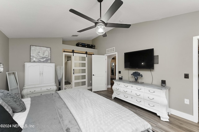 bedroom featuring ceiling fan, a barn door, dark wood-type flooring, and vaulted ceiling