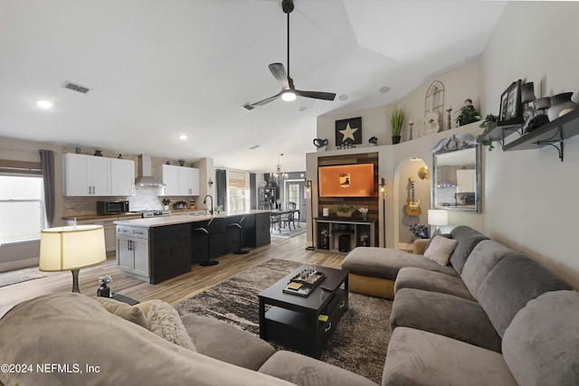 living room with ceiling fan with notable chandelier, light hardwood / wood-style floors, lofted ceiling, and sink