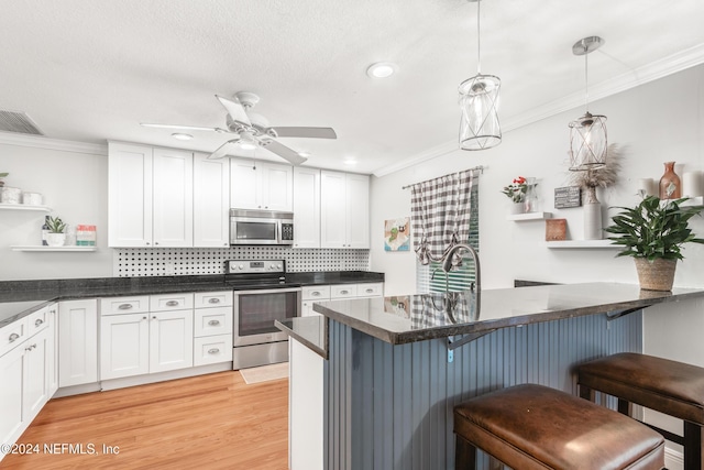 kitchen with appliances with stainless steel finishes, a breakfast bar, light hardwood / wood-style flooring, white cabinets, and hanging light fixtures