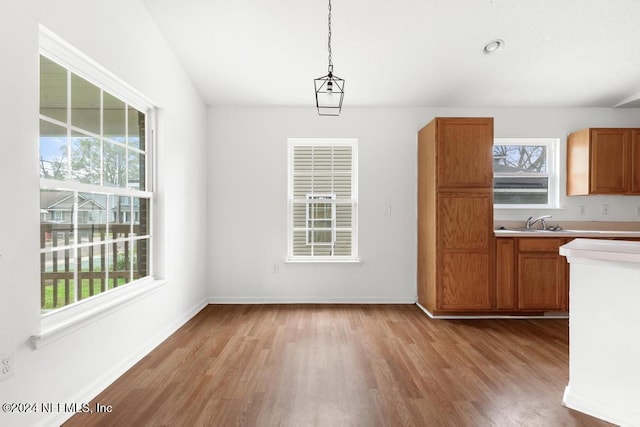 kitchen with a wealth of natural light, light wood-type flooring, hanging light fixtures, and sink