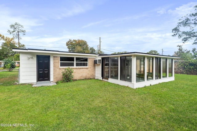 rear view of property featuring a sunroom, a wall mounted AC, and a lawn