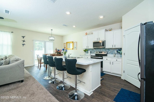 kitchen featuring a kitchen island with sink, hanging light fixtures, appliances with stainless steel finishes, dark hardwood / wood-style flooring, and white cabinetry