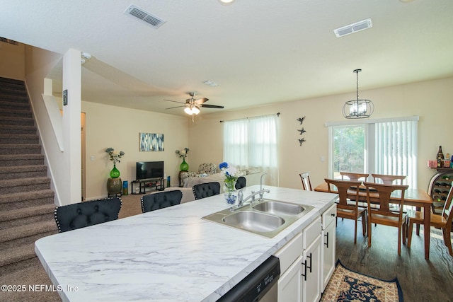 kitchen featuring a center island with sink, ceiling fan with notable chandelier, sink, decorative light fixtures, and white cabinetry