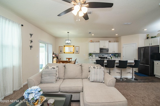 living room with ceiling fan, dark carpet, and a textured ceiling