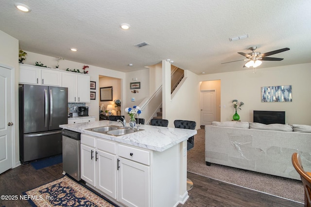 kitchen with appliances with stainless steel finishes, a textured ceiling, sink, a center island with sink, and white cabinets