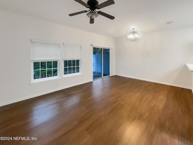 empty room with dark wood-type flooring and ceiling fan with notable chandelier