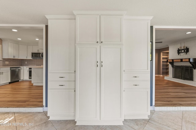 kitchen with backsplash, white cabinets, crown molding, light tile patterned flooring, and stainless steel appliances