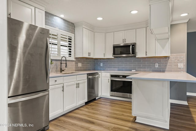 kitchen featuring white cabinetry, sink, stainless steel appliances, kitchen peninsula, and light wood-type flooring