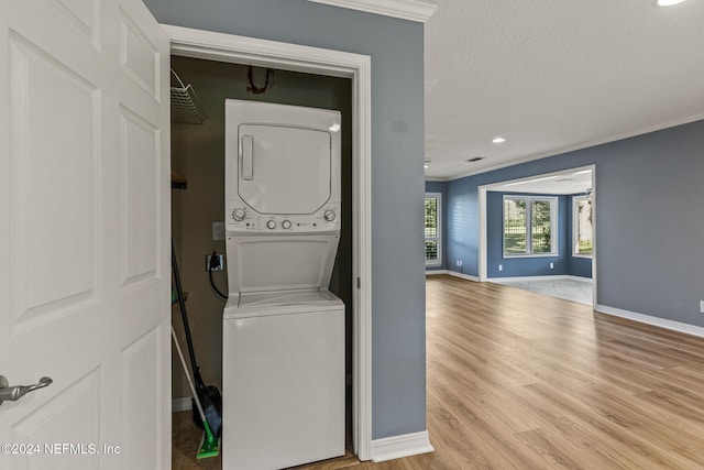 laundry area with a textured ceiling, crown molding, stacked washer / dryer, and light hardwood / wood-style flooring