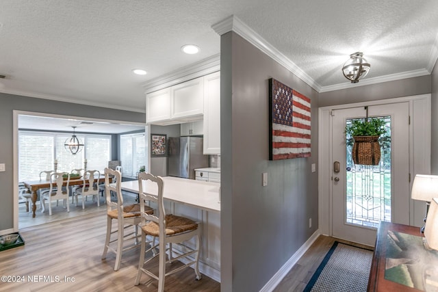 kitchen with stainless steel fridge, ornamental molding, a textured ceiling, light hardwood / wood-style flooring, and white cabinets