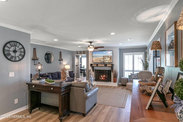 living room featuring a stone fireplace, crown molding, light hardwood / wood-style flooring, and ceiling fan