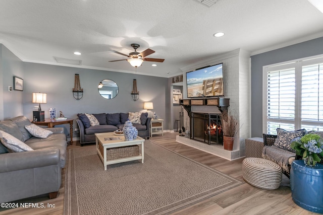 living room with crown molding, a brick fireplace, ceiling fan, a textured ceiling, and wood-type flooring