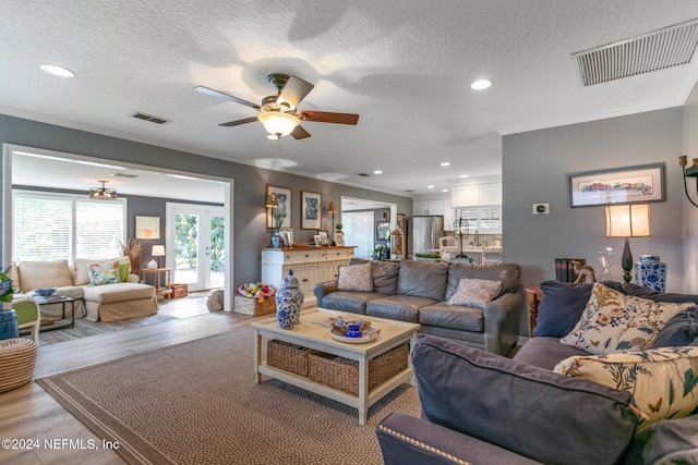 living room with a textured ceiling, light hardwood / wood-style flooring, ceiling fan, and crown molding