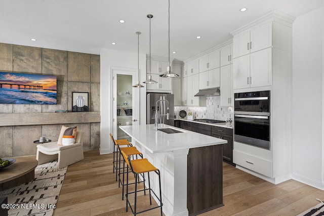 kitchen with decorative light fixtures, white cabinets, appliances with stainless steel finishes, and an island with sink