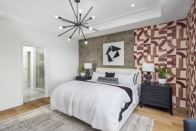 bedroom with connected bathroom, light hardwood / wood-style floors, ornamental molding, a raised ceiling, and a chandelier