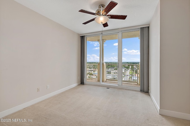 carpeted spare room with expansive windows and ceiling fan