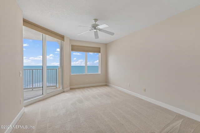 spare room with ceiling fan, a water view, light colored carpet, and a textured ceiling