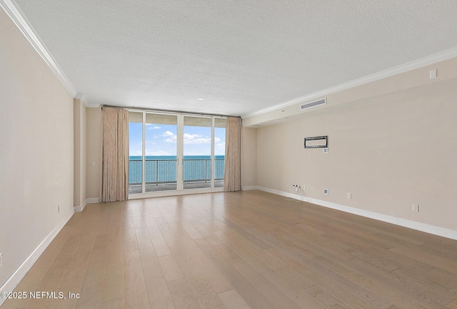 empty room with a textured ceiling, crown molding, wood-type flooring, a water view, and a wall of windows