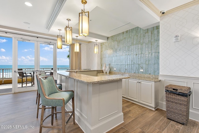 kitchen featuring light stone countertops, dark hardwood / wood-style flooring, decorative light fixtures, a water view, and white cabinetry