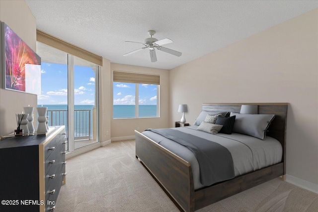 bedroom with a water view, ceiling fan, access to exterior, a textured ceiling, and light colored carpet