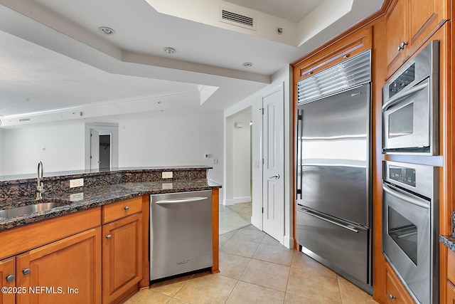 kitchen with visible vents, a tray ceiling, a sink, stainless steel appliances, and brown cabinets