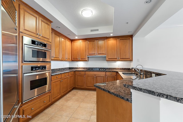 kitchen featuring visible vents, a tray ceiling, brown cabinets, appliances with stainless steel finishes, and a sink