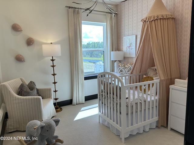 bedroom featuring an inviting chandelier, a crib, and light carpet