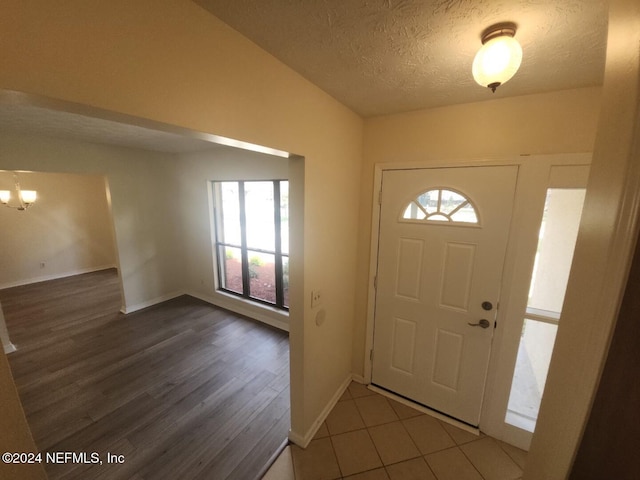 foyer entrance featuring dark wood-style floors, baseboards, a chandelier, and a textured ceiling